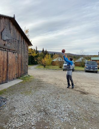 Dylan playing basketball with a hoop on a worn out barn